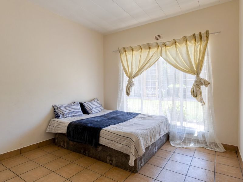 A simple bedroom featuring tiled flooring and a large window that allows for natural light.