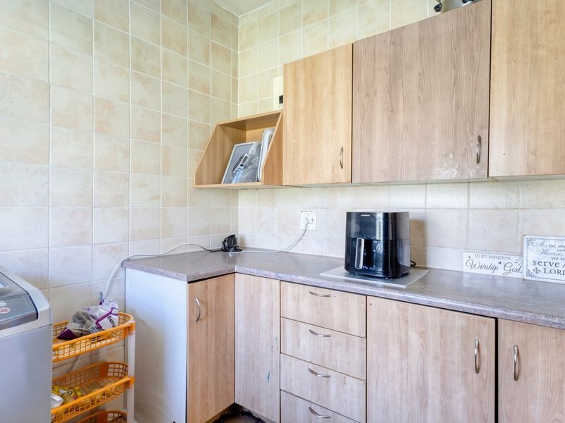 A functional laundry area featuring laminate cabinetry, ample countertop space, and full-height ceramic wall tiling.