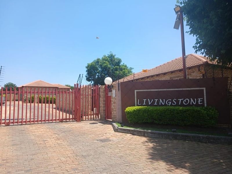 Front entrance view of the Livingstone complex featuring a secure gated access point, brick perimeter wall, and paved driveway.