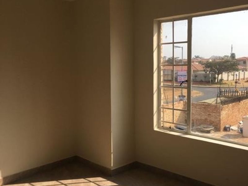 A bright, empty bedroom featuring modern tiled flooring and a large grid-pattern window with natural light.