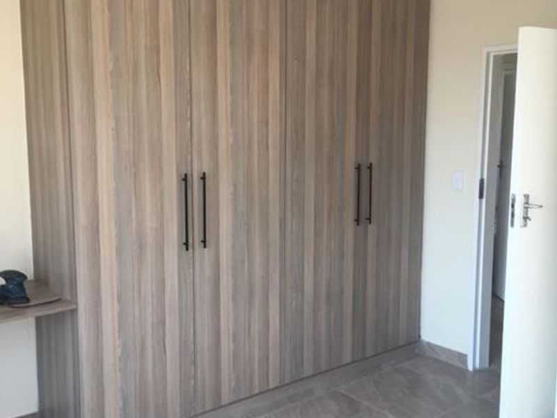 A clean bedroom featuring modern wood-grain built-in cupboards and contemporary large-format floor tiles.