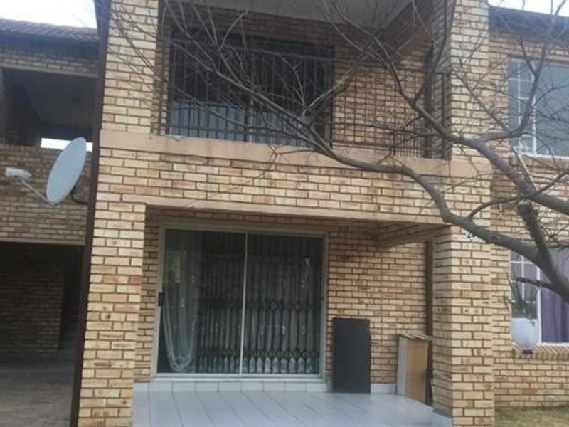 Two-story face brick apartment exterior featuring a ground floor tiled patio with sliding doors and an upper-level balcony.