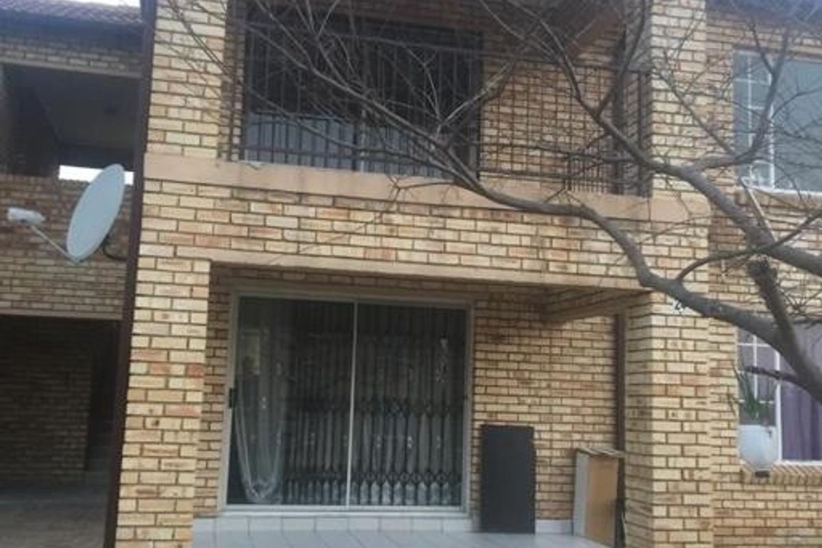 Two-story face brick apartment exterior featuring a ground floor tiled patio with sliding doors and an upper-level balcony.