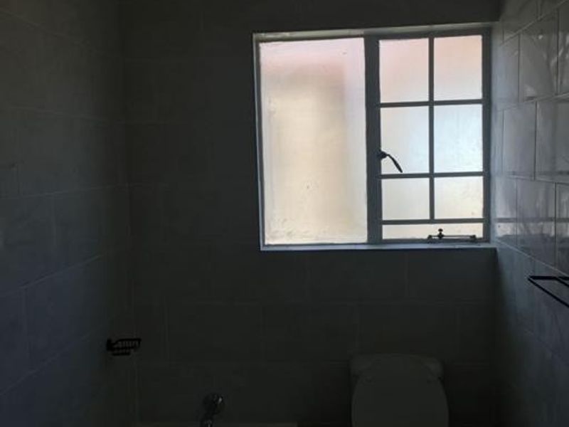 A functional bathroom featuring a bathtub, toilet, and tiled walls, illuminated by a window with security bars.