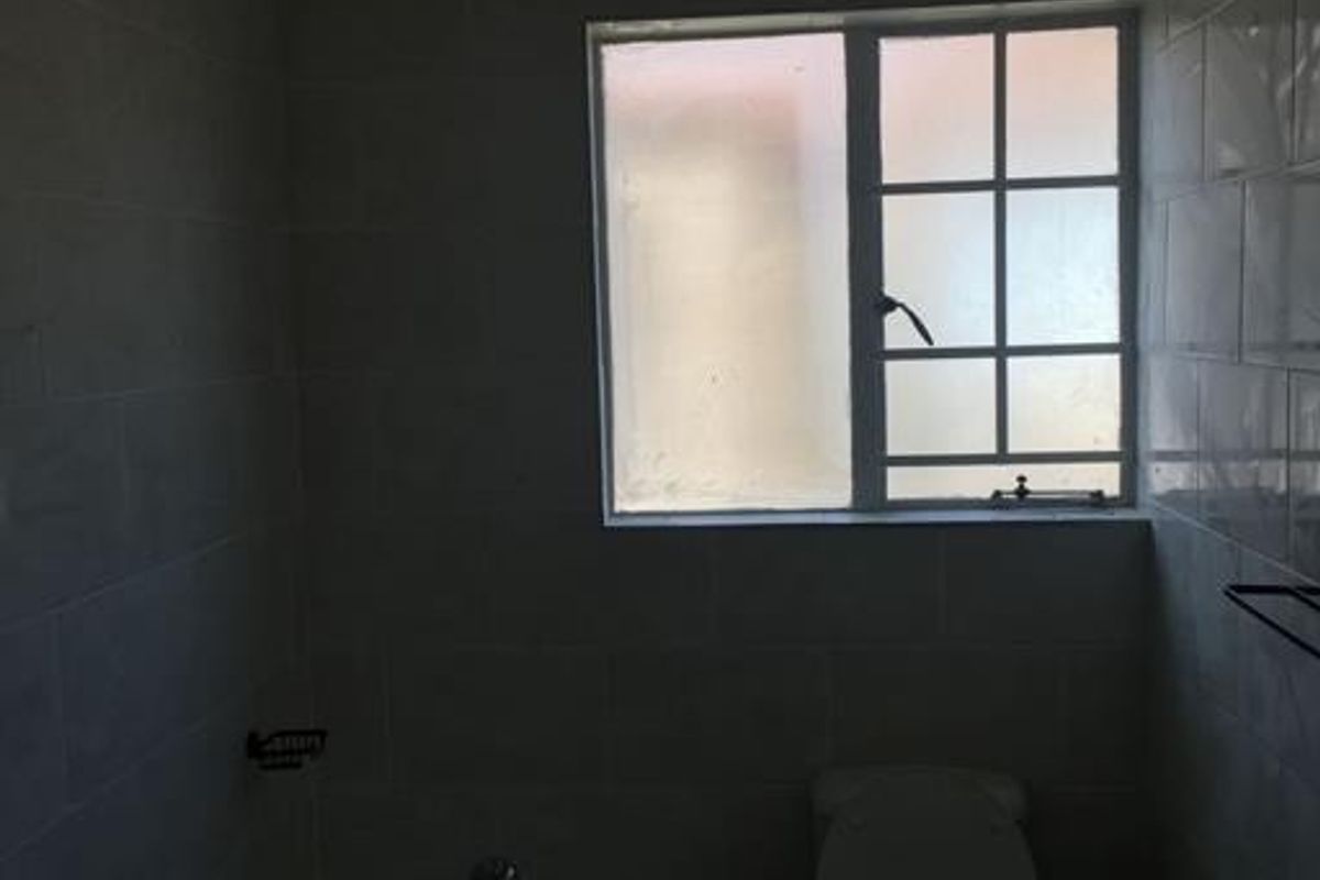 A functional bathroom featuring a bathtub, toilet, and tiled walls, illuminated by a window with security bars.