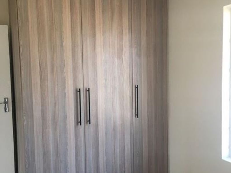 A clean bedroom featuring modern wood-finish built-in cupboards and neutral tiled flooring, offering a bright and functional storage space.