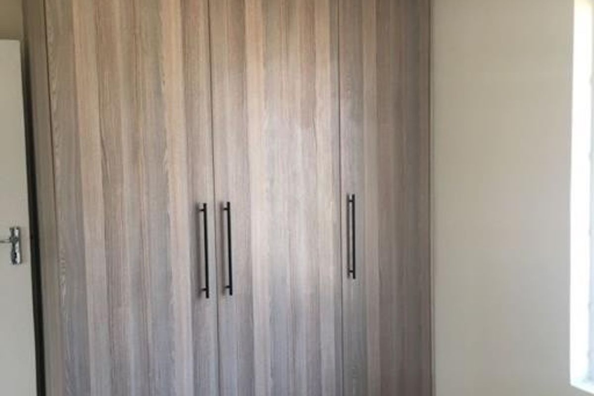 A clean bedroom featuring modern wood-finish built-in cupboards and neutral tiled flooring, offering a bright and functional storage space.