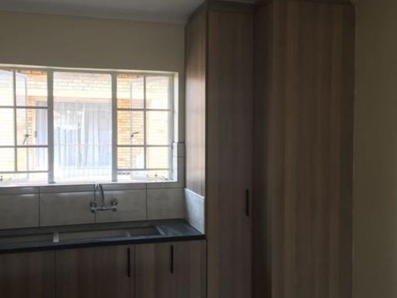A functional kitchen area featuring modern wood-look cabinetry, dark laminate countertops, a stainless steel sink, and a window providing natural light.