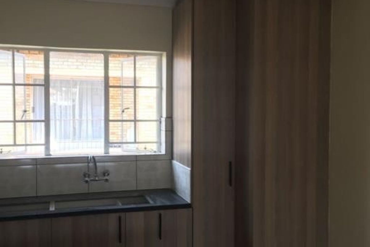 A functional kitchen area featuring modern wood-look cabinetry, dark laminate countertops, a stainless steel sink, and a window providing natural light.