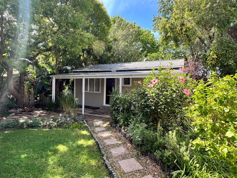 A charming rear exterior view featuring a covered veranda, stone pathway, and established garden surroundings.