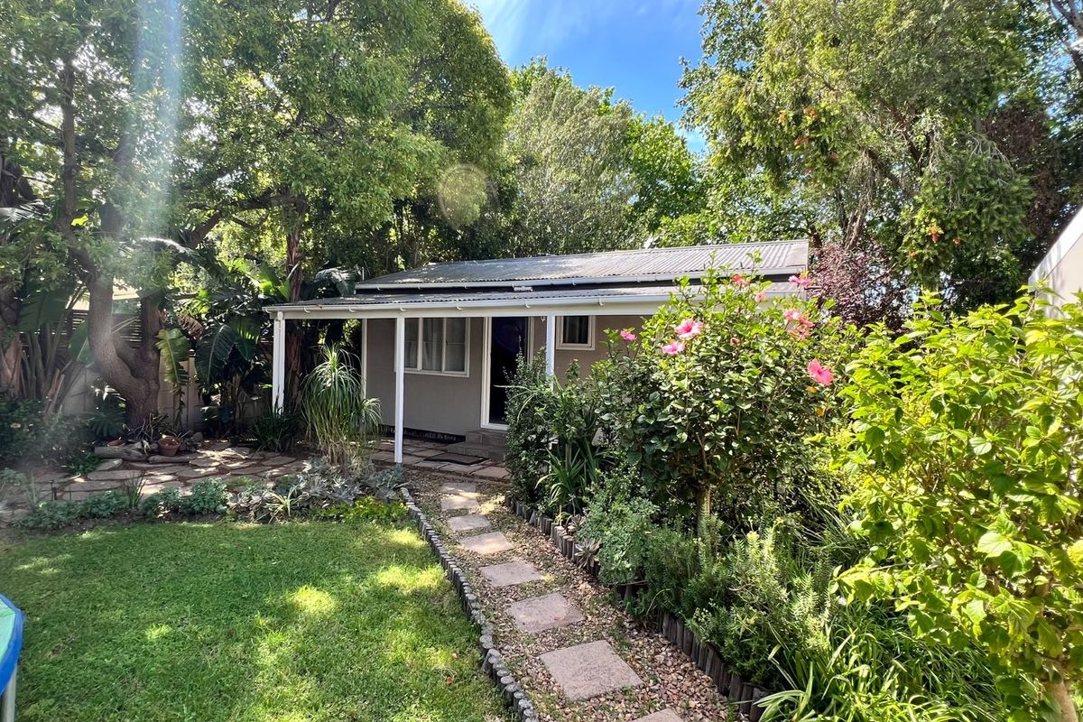 A charming rear exterior view featuring a covered veranda, stone pathway, and established garden surroundings.