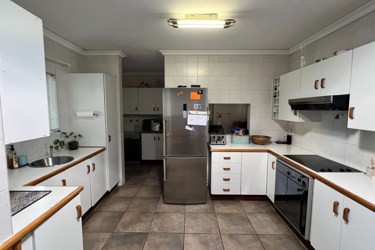 A functional kitchen featuring white cabinetry, laminate countertops, tiled walls, and integrated appliances, offering a practical layout with potential for modern updates.