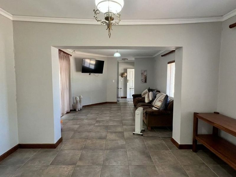 Spacious open-plan living area featuring neutral wall tones, tiled flooring, and large windows with venetian blinds, offering a versatile layout for family living.