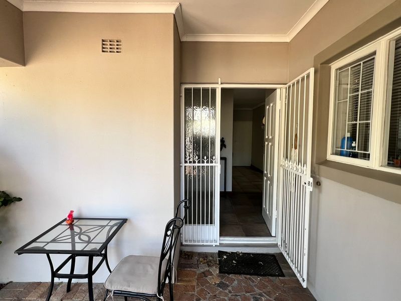 A covered patio area featuring a security gate entrance, tiled flooring, and a window with burglar bars, providing a functional outdoor transition space.