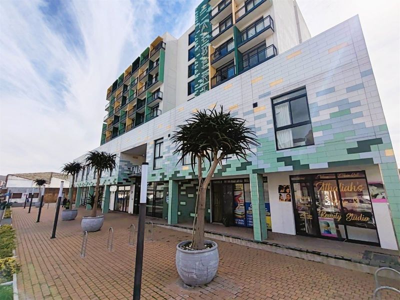 Exterior view of a modern apartment building featuring a decorative tiled facade, ground-floor commercial spaces, and a paved pedestrian walkway.