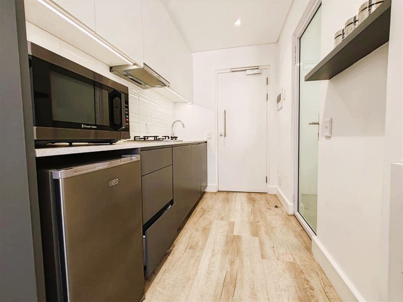 Modern, compact kitchen featuring sleek handleless cabinetry, stone countertops, subway tile backsplash, and integrated lighting, finished with durable wood-look laminate flooring.