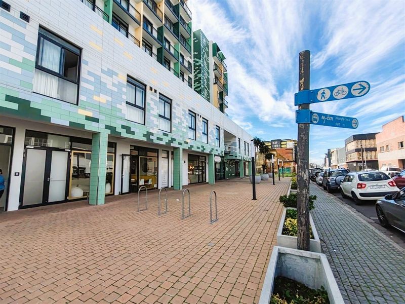 Exterior view of the apartment building facade featuring modern tiled finishes, paved pedestrian walkway, and convenient street-level bicycle racks.