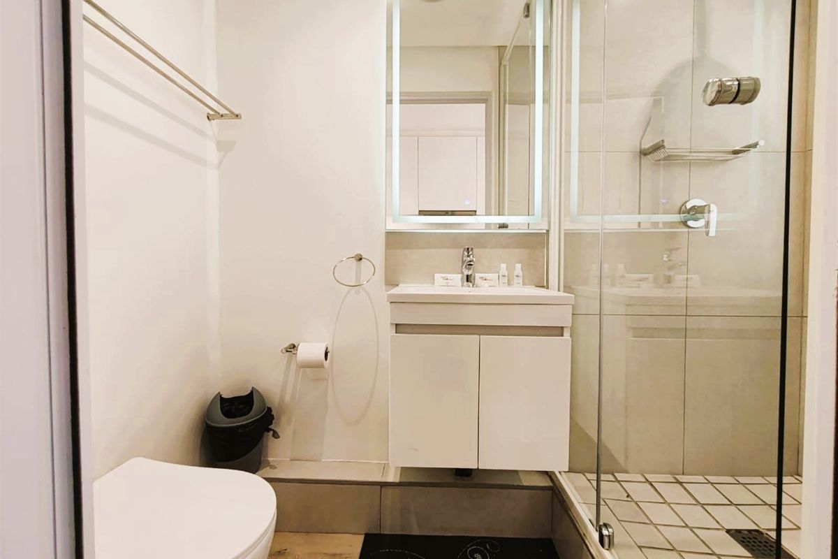 Modern bathroom featuring a wall-mounted vanity, illuminated mirror, and a glass-enclosed shower with tiled flooring.