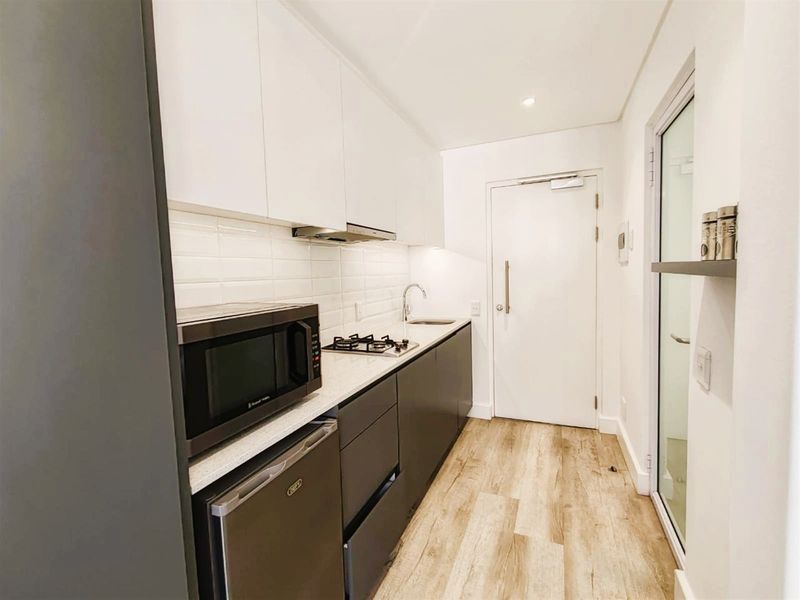 Modern galley-style kitchen featuring sleek white and dark grey cabinetry, stone countertops, subway tile backsplash, and integrated gas hob with extractor fan.