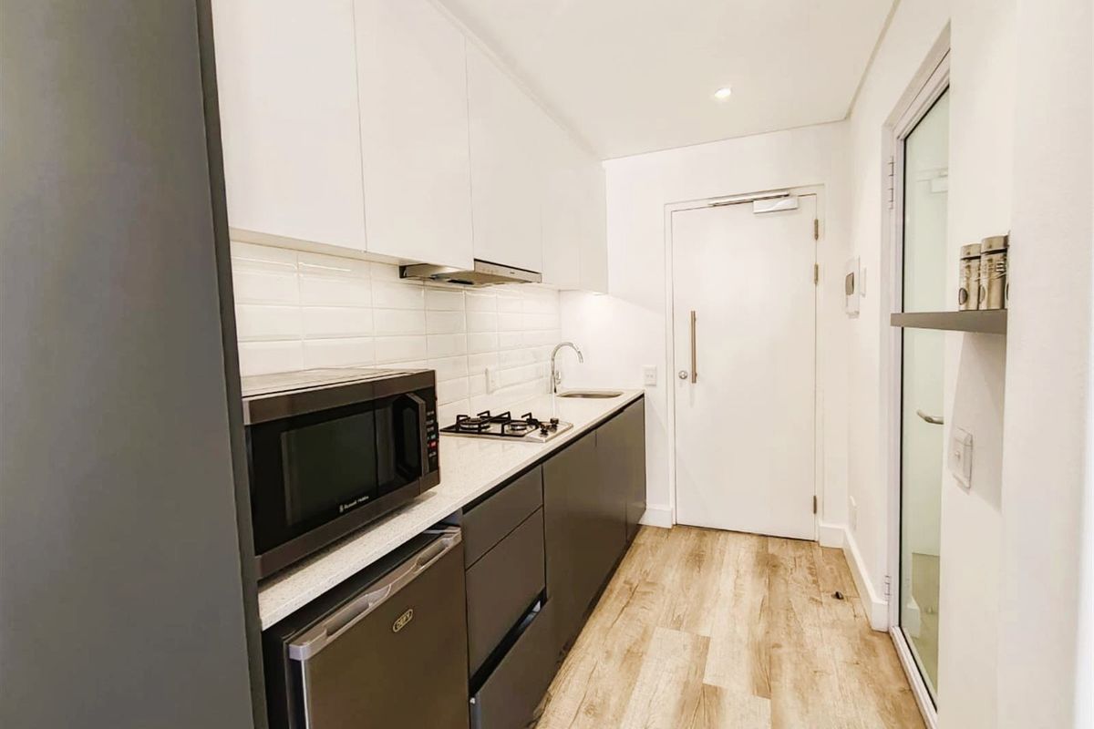 Modern galley-style kitchen featuring sleek white and dark grey cabinetry, stone countertops, subway tile backsplash, and integrated gas hob with extractor fan.