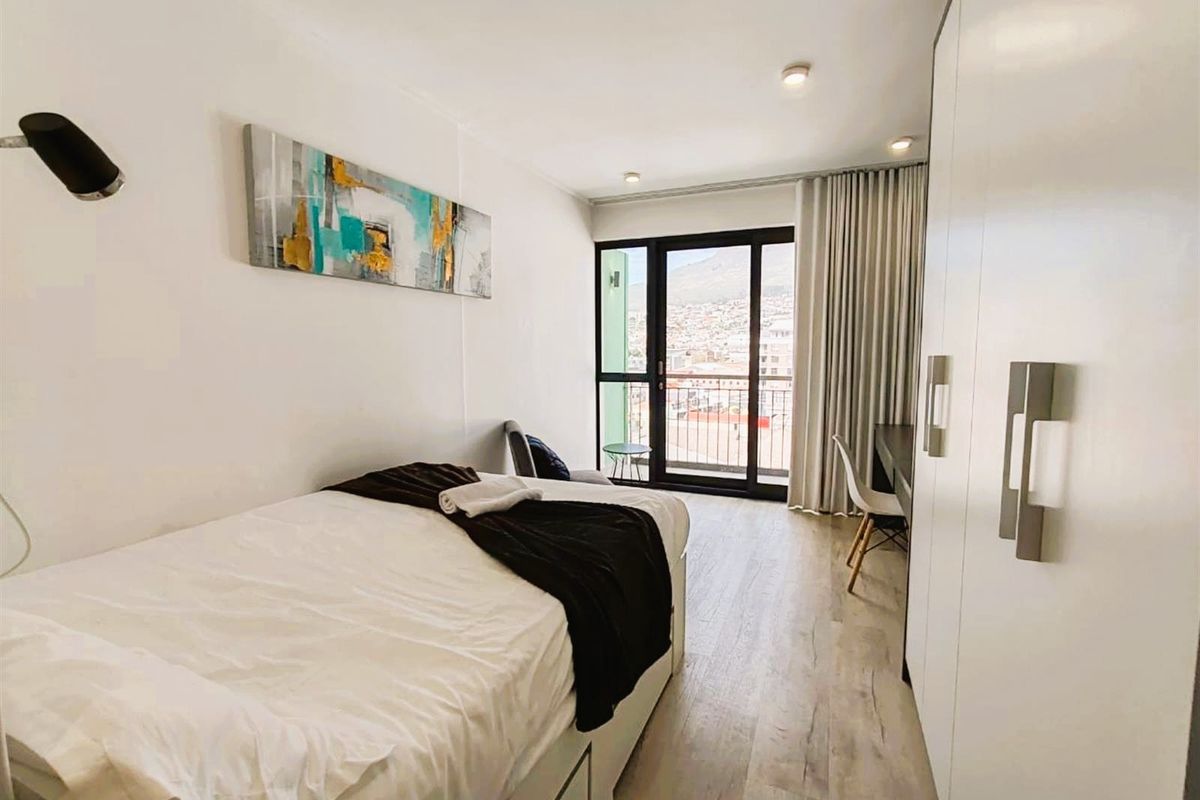 Modern bedroom featuring light laminate flooring, built-in wardrobes, and a sliding glass door leading to a balcony with city views.