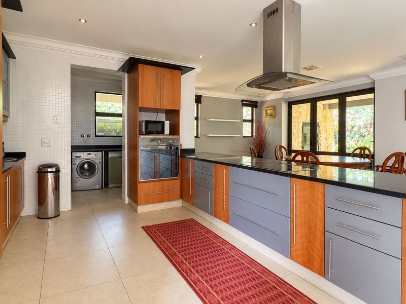 Spacious kitchen featuring a large island with granite countertops, built-in oven, extractor fan, and an adjacent scullery area with laundry facilities.