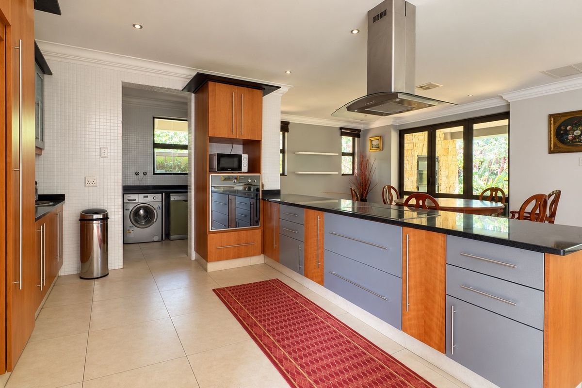 Spacious kitchen featuring a large island with granite countertops, built-in oven, extractor fan, and an adjacent scullery area with laundry facilities.