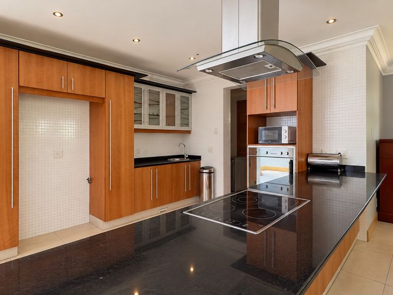 Modern kitchen featuring wood-finish cabinetry, black granite countertops, integrated electric hob, built-in oven, and a stainless steel extractor fan.