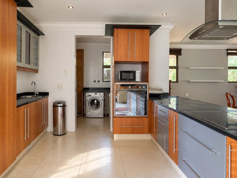 Modern kitchen featuring warm wood cabinetry, granite countertops, integrated appliances, and a functional layout with an adjacent scullery area.