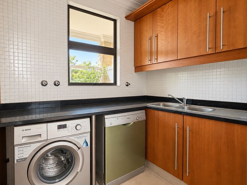 A functional laundry room featuring built-in wooden cabinetry, a double sink, black granite countertops, and tiled backsplash with space for appliances.