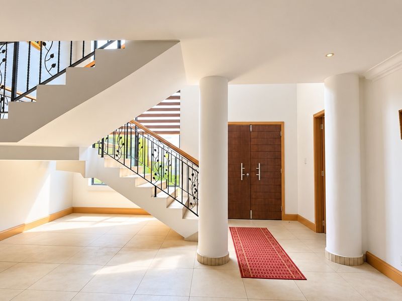 Spacious entrance hall featuring a grand curved staircase with wrought iron balustrade, double timber doors, and elegant structural columns.