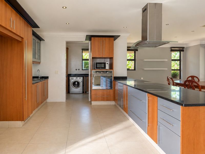 Spacious open-plan kitchen featuring modern wood and grey cabinetry, granite countertops, integrated appliances, and a seamless flow into the dining area.