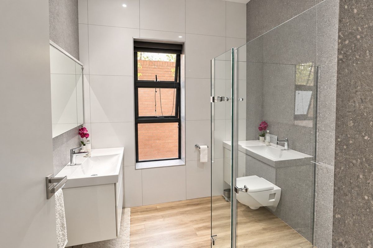 Modern bathroom featuring a wall-mounted vanity, wall-hung toilet, glass shower enclosure, and contemporary tiled finishes with wood-look flooring.