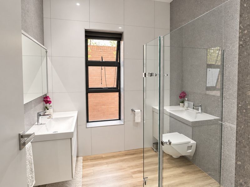 Modern bathroom featuring a wall-mounted vanity, wall-hung toilet, glass shower enclosure, and contemporary tiled finishes with wood-look flooring.