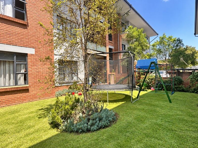A view of the rear exterior of the apartment building, featuring a well-maintained lawn, landscaped garden beds, and brick facade.