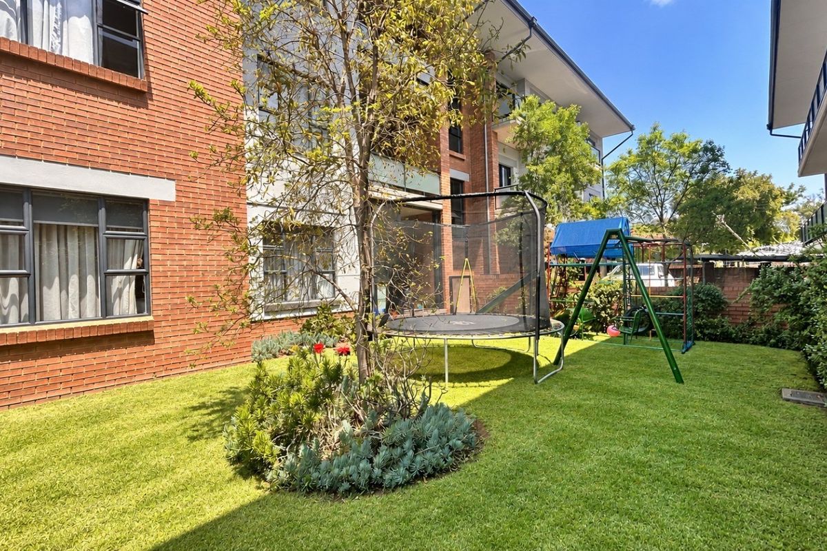 A view of the rear exterior of the apartment building, featuring a well-maintained lawn, landscaped garden beds, and brick facade.