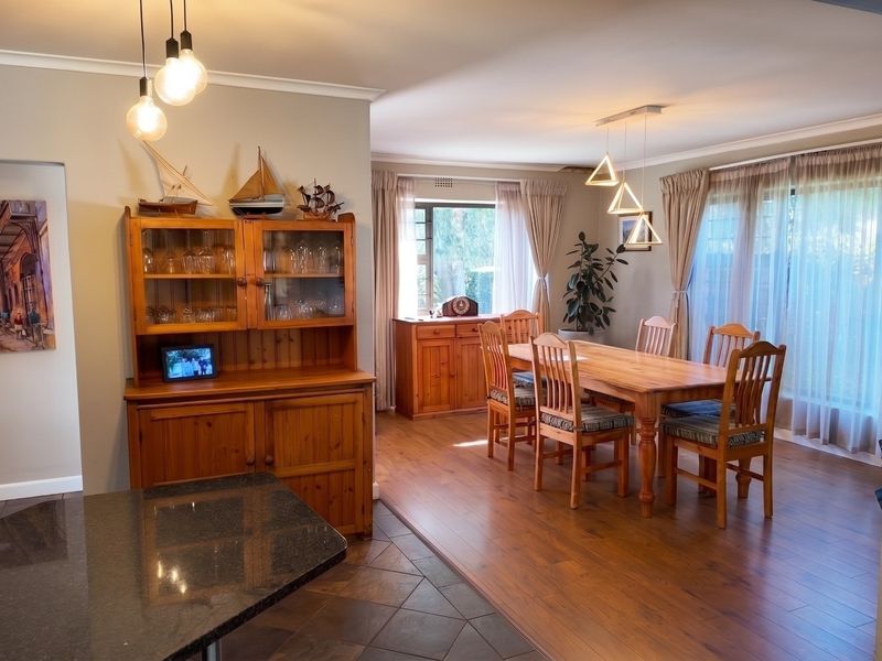 Spacious open-plan dining area featuring a blend of tiled and laminate flooring, modern pendant lighting, and large windows with natural light.