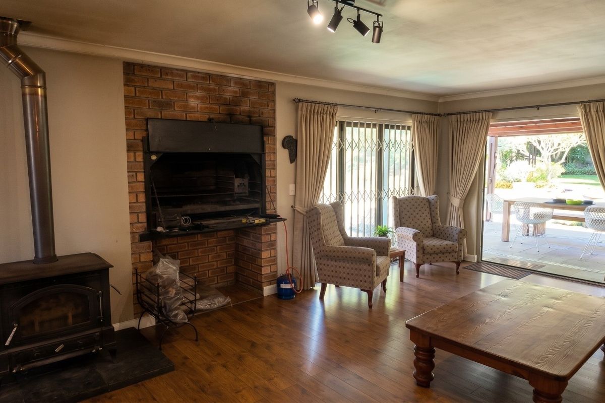 Spacious living room featuring a brick fireplace with built-in braai, a wood-burning stove, laminate flooring, and sliding doors leading to an outdoor patio area.
