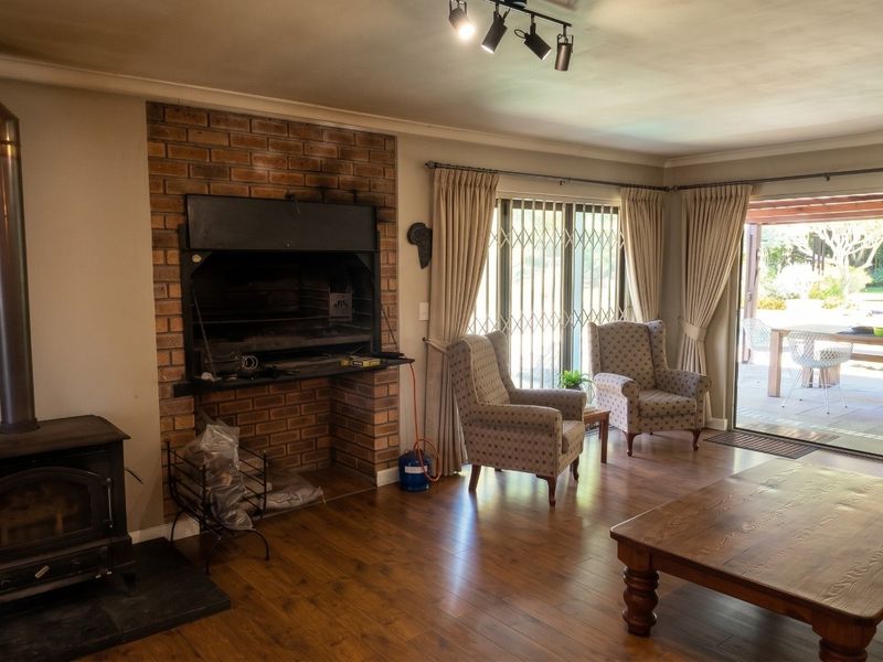 Spacious living room featuring a brick fireplace with built-in braai, a wood-burning stove, laminate flooring, and sliding doors leading to an outdoor patio area.