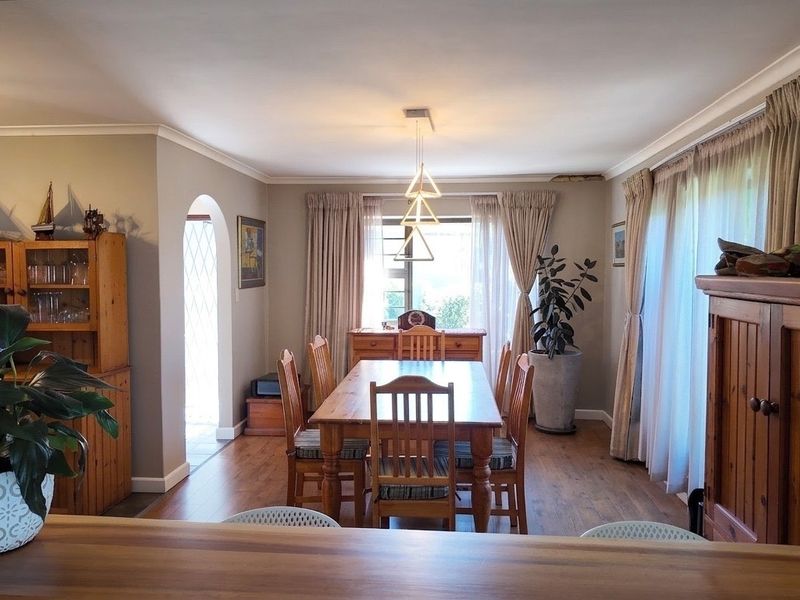 A dining room featuring laminate flooring, an arched entryway, and a decorative pendant light fixture, with natural light provided by large windows.