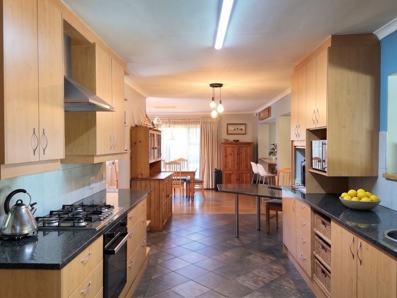Open-plan kitchen featuring light wood cabinetry, granite countertops, gas hob, and integrated oven, flowing into a dining area with tiled flooring.