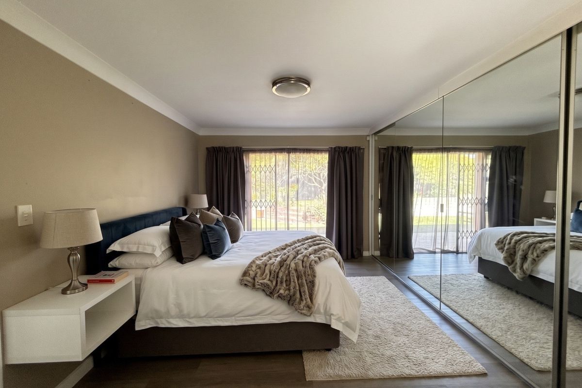 Spacious bedroom featuring laminate flooring, a large built-in mirrored wardrobe, and sliding glass doors with security gates leading to the exterior.