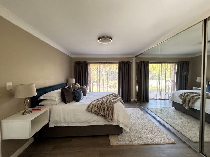 Spacious bedroom featuring laminate flooring, a large built-in mirrored wardrobe, and sliding glass doors with security gates leading to the exterior.
