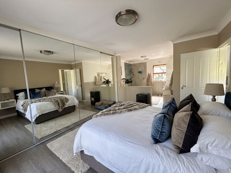 Spacious bedroom featuring large mirrored sliding wardrobes, laminate flooring, and an open-plan en-suite bathroom area with modern finishes.