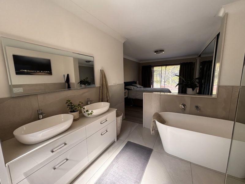 Modern open-plan en-suite bathroom featuring a double vanity with vessel sinks, a sleek freestanding bathtub, and contemporary neutral tiling.