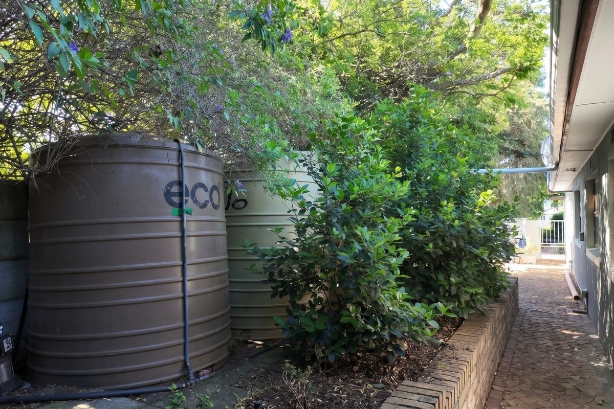 Side exterior area featuring two large water storage tanks, a water pump, a brick retaining wall, and a paved walkway.