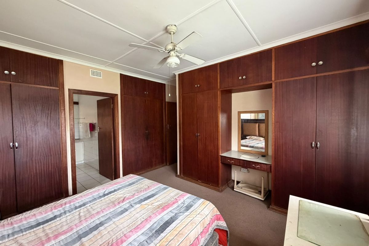 A bedroom featuring extensive built-in wooden cabinetry, a central ceiling fan, and an integrated vanity area, offering significant storage potential.