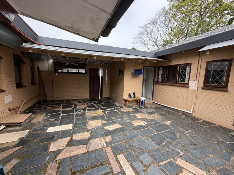 A covered rear patio area featuring flagstone paving and brick exterior walls, offering a functional outdoor space with potential for renovation and landscaping.