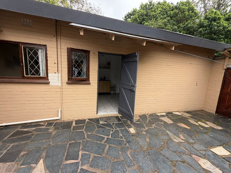 Rear exterior view of the property featuring a stone paved patio, brick walls, and leaded glass windows with access to the interior.