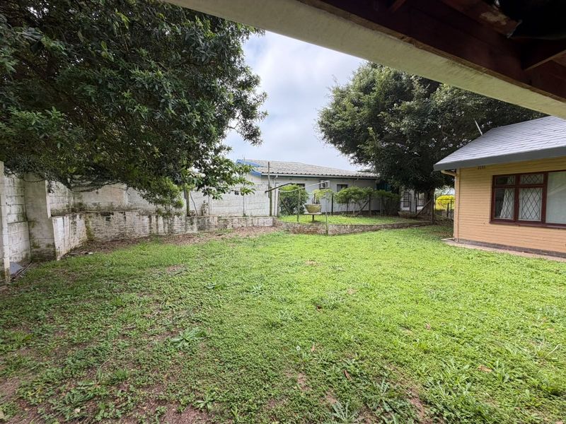 A spacious rear garden featuring a lawn area, retaining walls, and a view of the adjacent building structure.